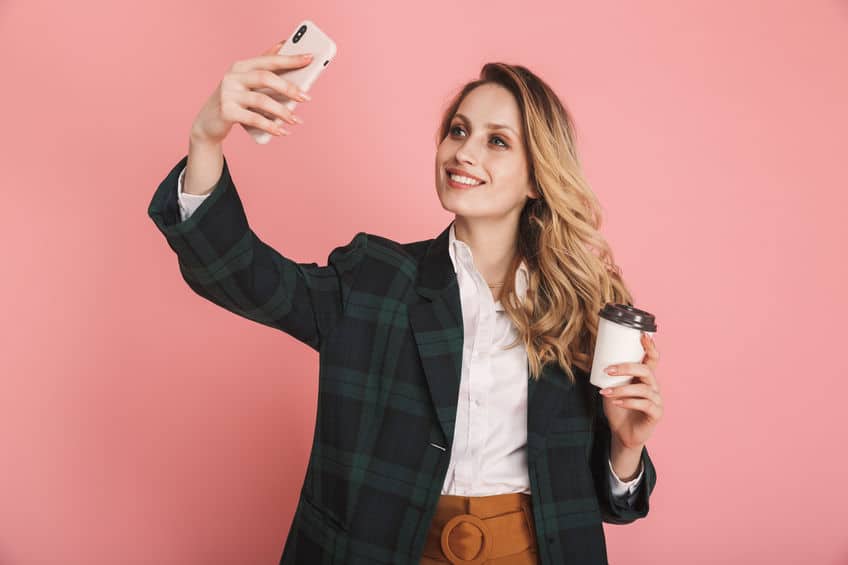Image of elegant woman 30s in trendy jacket using mobile phone and drinking takeaway coffee isolated over pink background